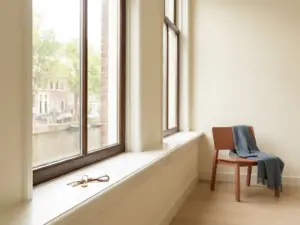 Polished house keys on a white windowsill in an Amsterdam canal apartment, with brick facades and water visible through tall Dutch windows.