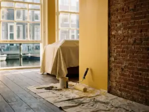 Half gerenoveerd interieur van Amsterdams grachtenpand met verse verf naast origineel metselwerk en verfroller op afdekdoek.