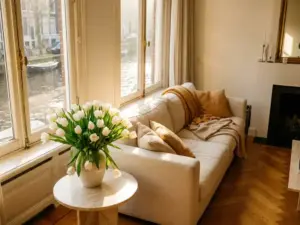 Witte tulpen op een marmeren bijzettafel in een Amsterdamse grachtenpandwoonkamer met visgraatparket en hoog raam met grachtzicht.