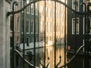 Luxe Amsterdams grachtenpand met witte raamkozijnen, gezien door een smeedijzeren poort in warm middaglicht.