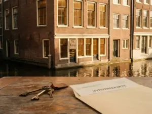 House keys on wood surface with Amsterdam canal house for sale and mortgage document in soft focus background.