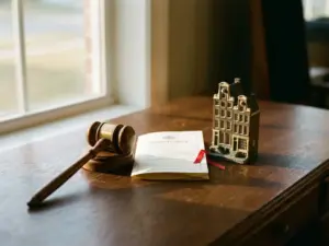 Weathered wooden gavel beside a property document and Dutch canal house scale model on a polished oak desk.